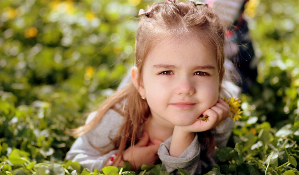 Красивая маленькая кареглазая девочка лежит на траве 