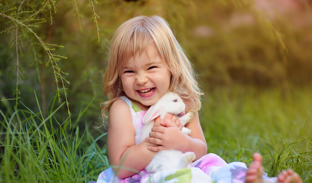 Довольная маленькая девочка обнимает белого кролика на траве 