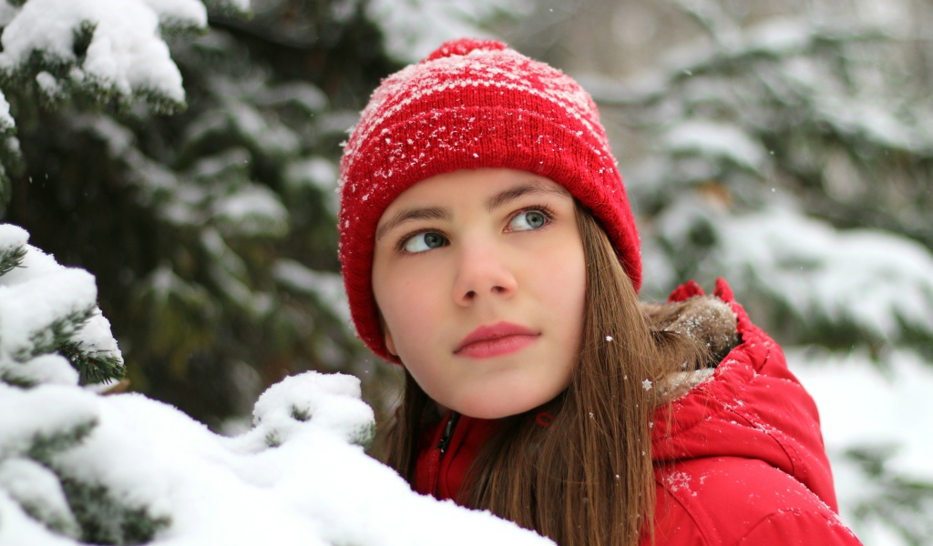 Милая девочка в красной шапке у заснеженной ели