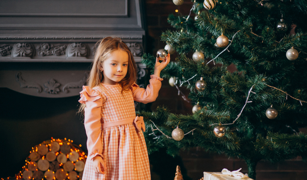 Милая маленькая девочка стоит у наряженной елки 