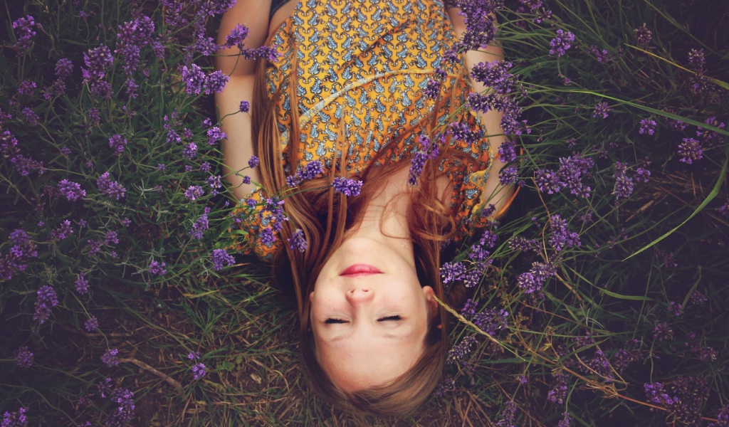 Девочка с закрытыми глазами лежит на земле с фиолетовыми  цветами