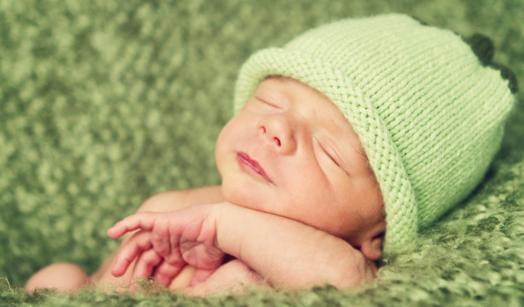 Зеленая вязаная шапка на голове у спящего ребенка 