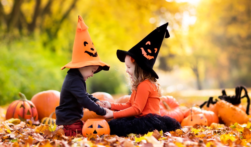 Маленькие мальчик и девочка в костюмах на Хэллоуин сидят на листве