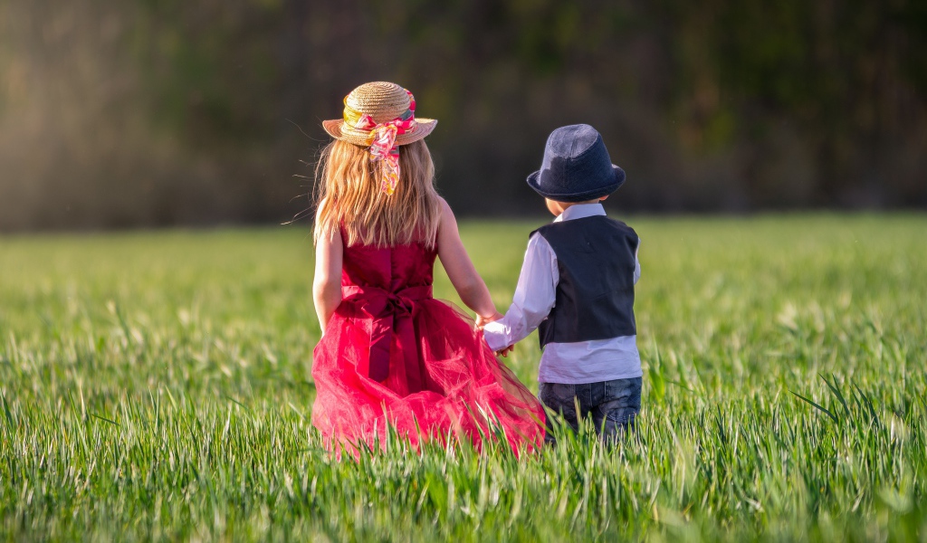 Маленькие мальчик и девочка идут по зеленому полю