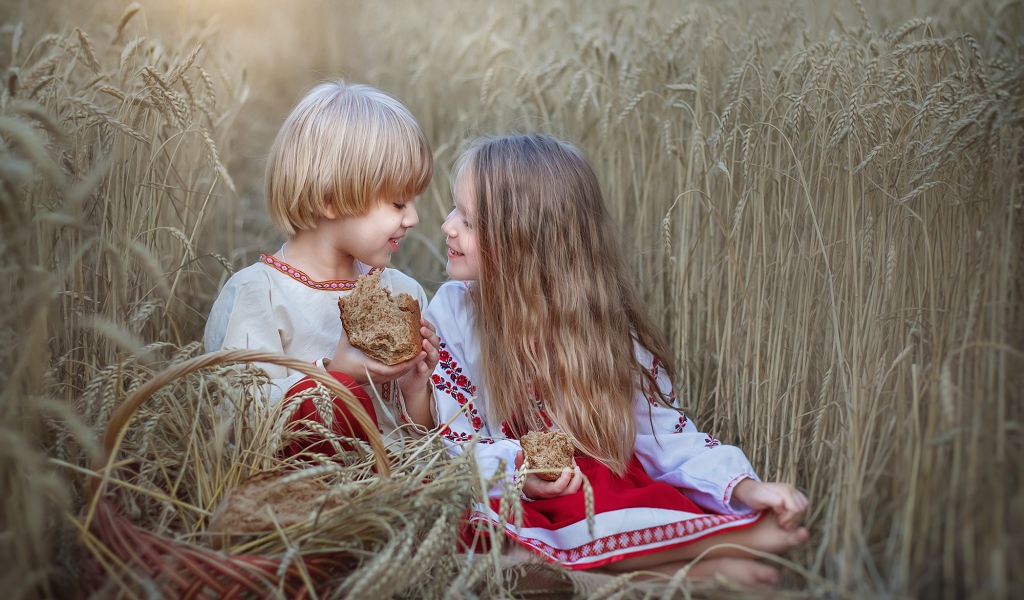Маленькие мальчик и девочка с хлебом на пшеничном поле 