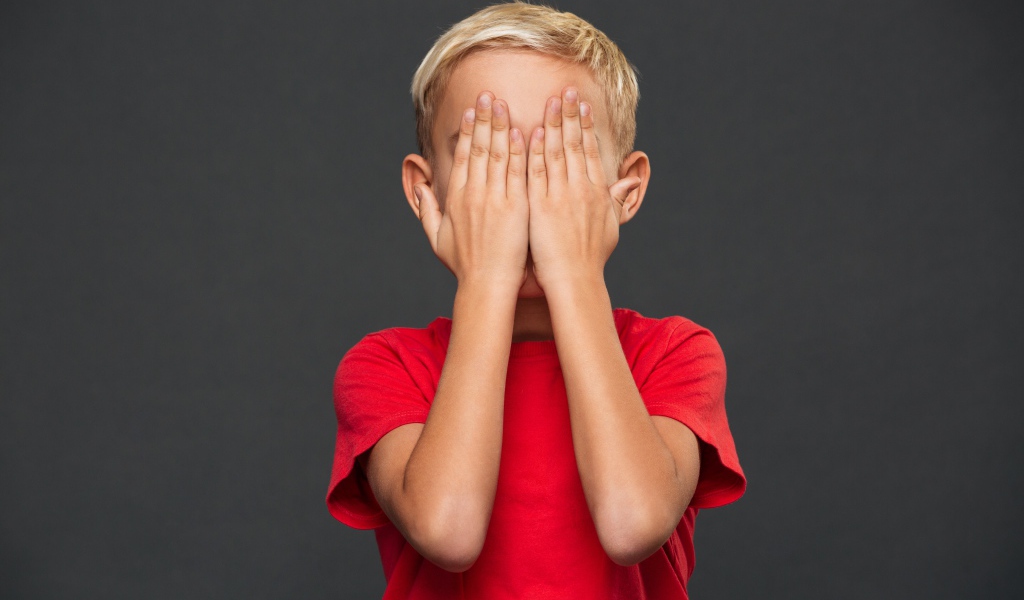 Маленький мальчик в красной футболке закрыл лицо руками 