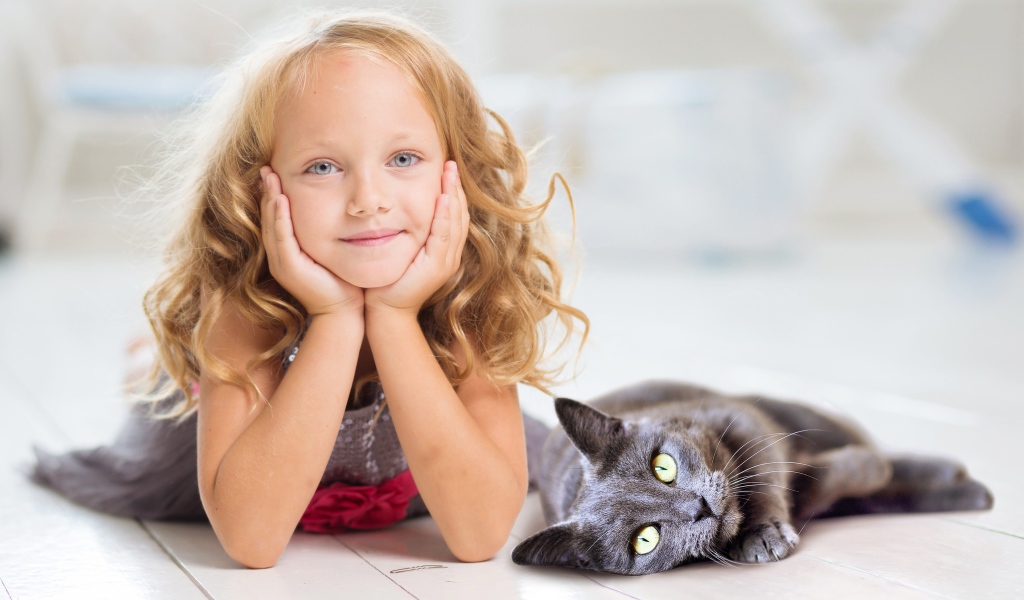 Маленькая милая голубоглазая девочка лежит на полу с котом