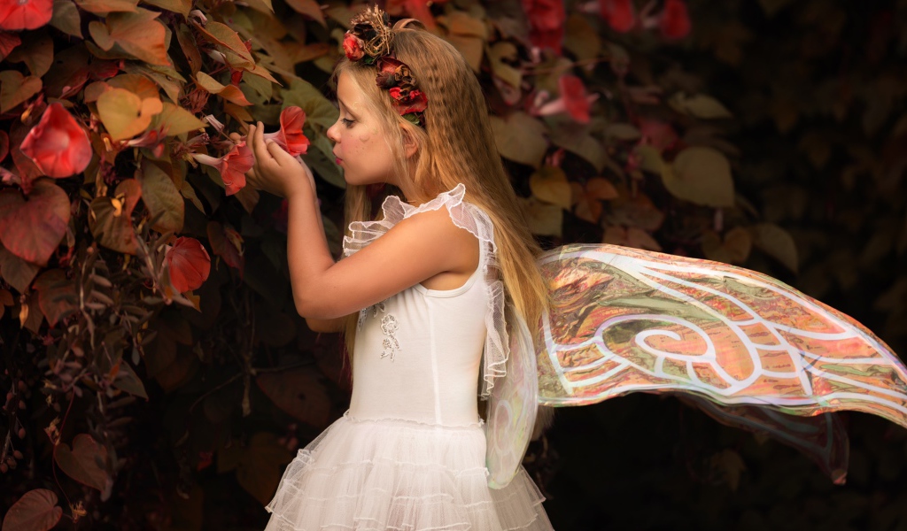 Маленькая девочка в костюме феи стоит у цветов