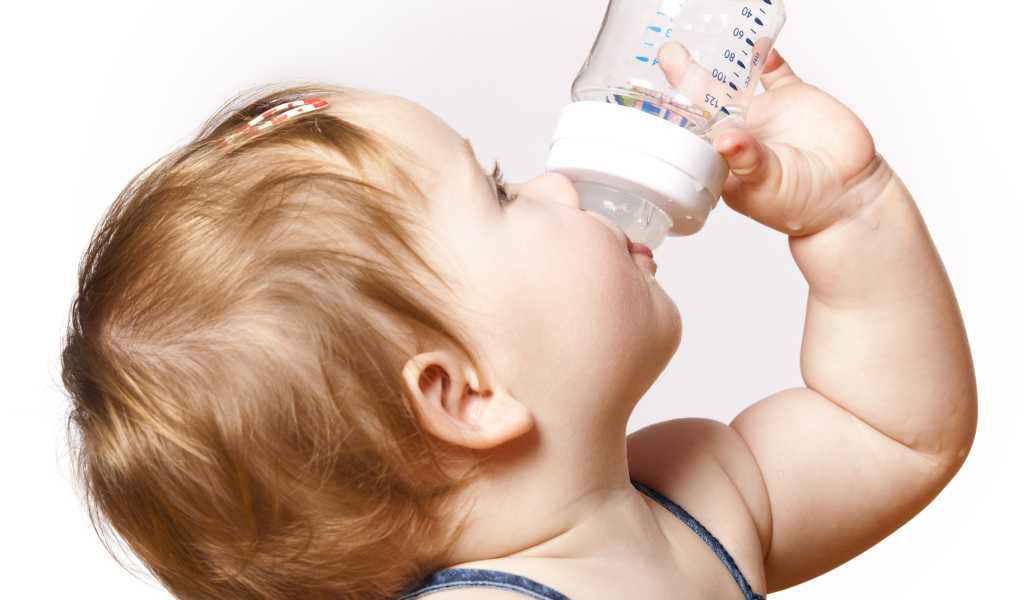 Маленькая девочка пьет молоко с бутылочки на белом фоне