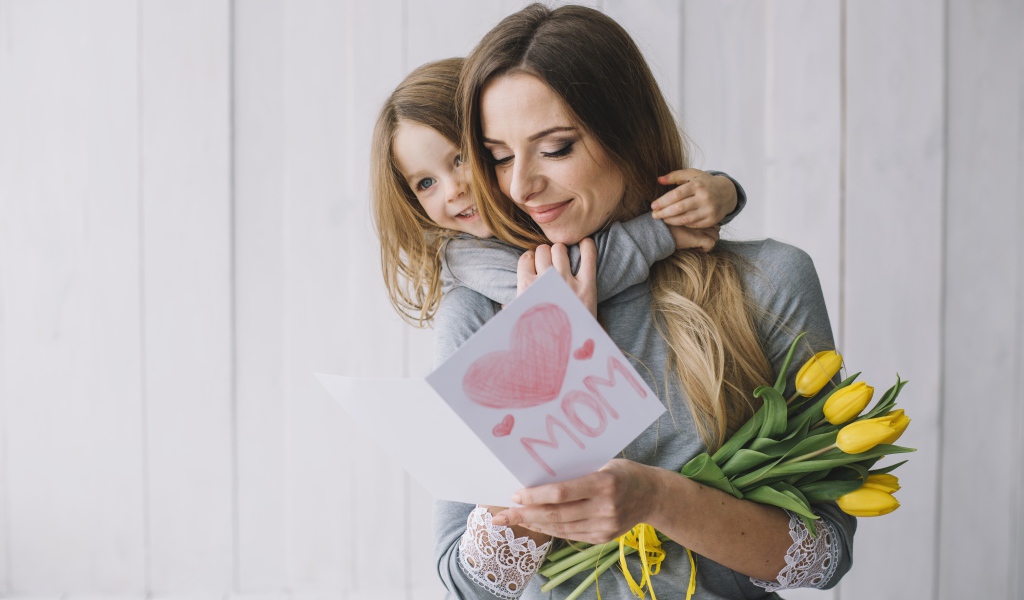 Маленькая девочка подарила маме открытку и букет тюльпанов