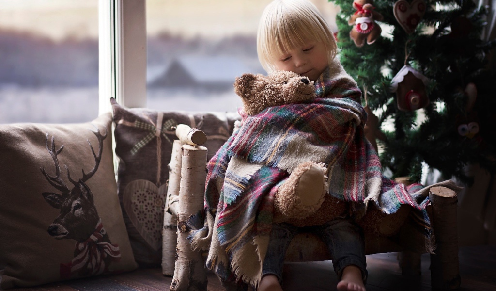 Маленькая девочка обнимает мишку у ели