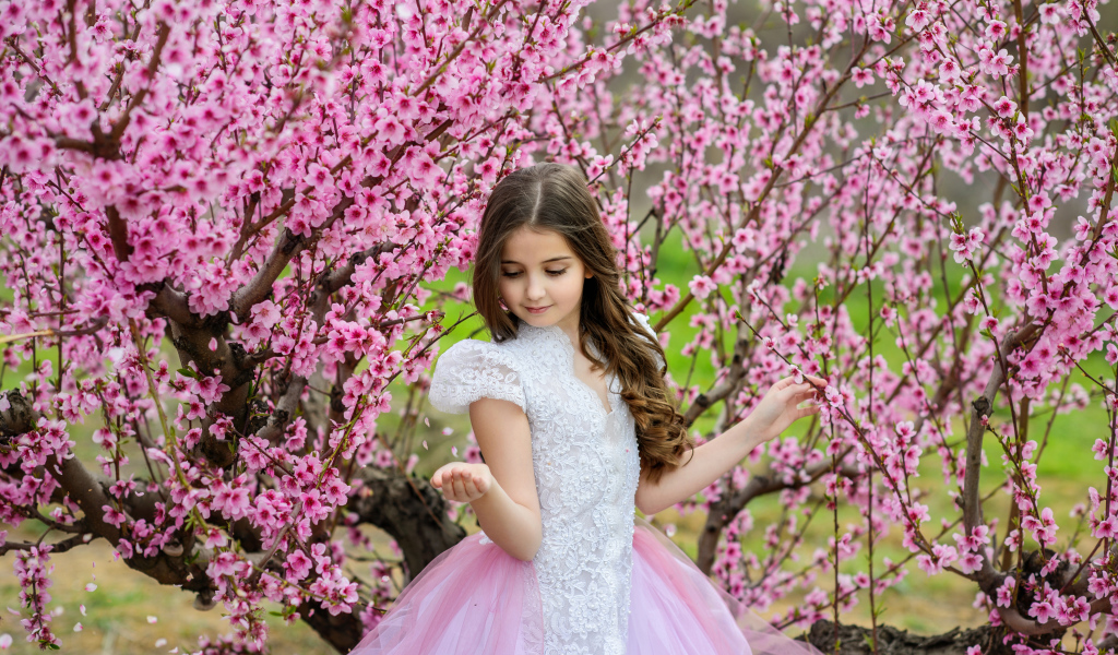 Маленькая девочка в красивом платье у дерева с розовыми цветами