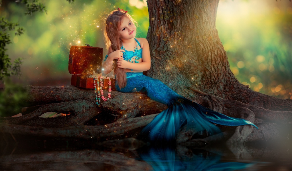 Маленькая девочка в костюме русалочки сидит у воды 