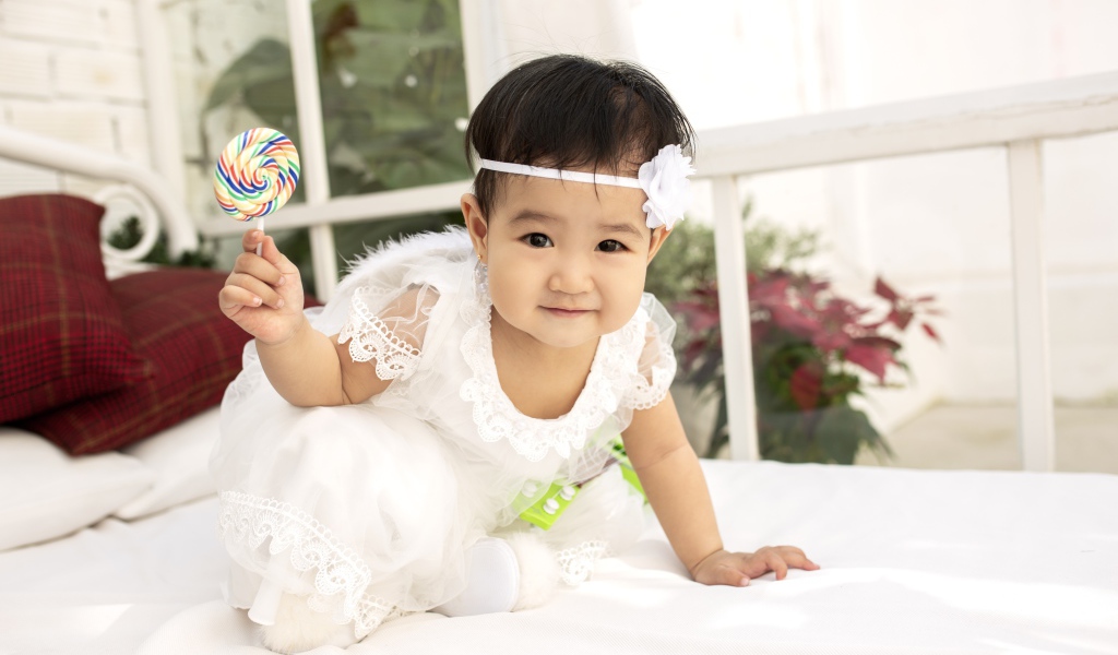 Маленькая девочка в белом платье с леденцом в руке