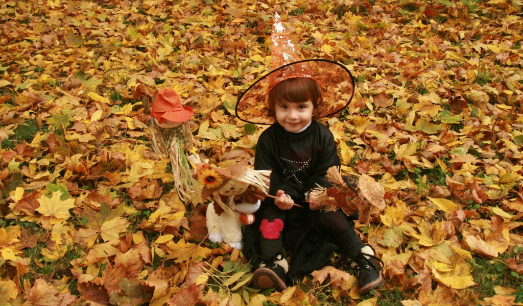 Маленькая девочка в костюме ведьмы сидит на опавшей листве на Хэллоуин