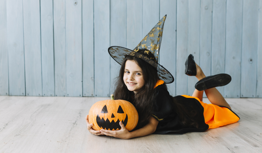Маленькая девочка в костюме ведьмы с тыквой на Хэллоуин