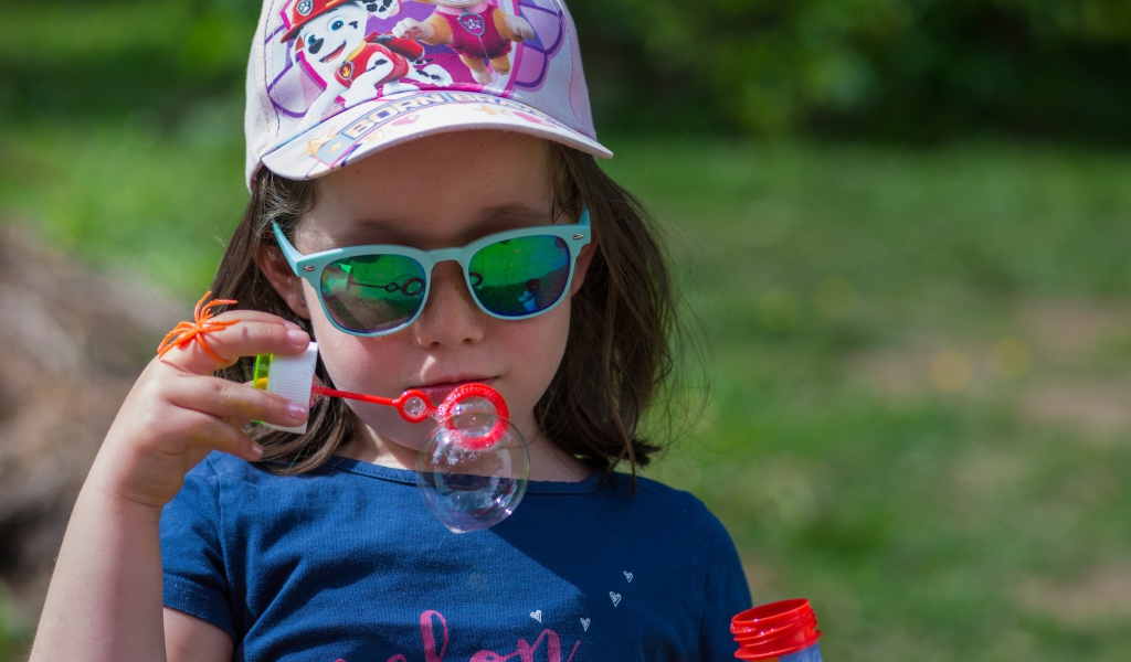 Маленькая девочка в очках с мыльными пузырями