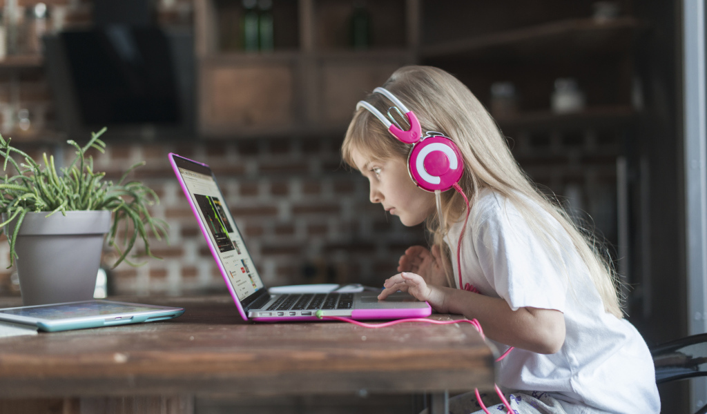 Маленькая девочка в наушниках сидит за ноутбуком