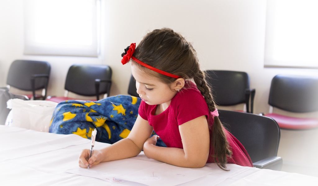 Маленькая девочка в красном платье рисует за столом