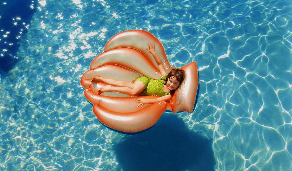 Маленькая девочка на надувном матрасе в бассейне летом 