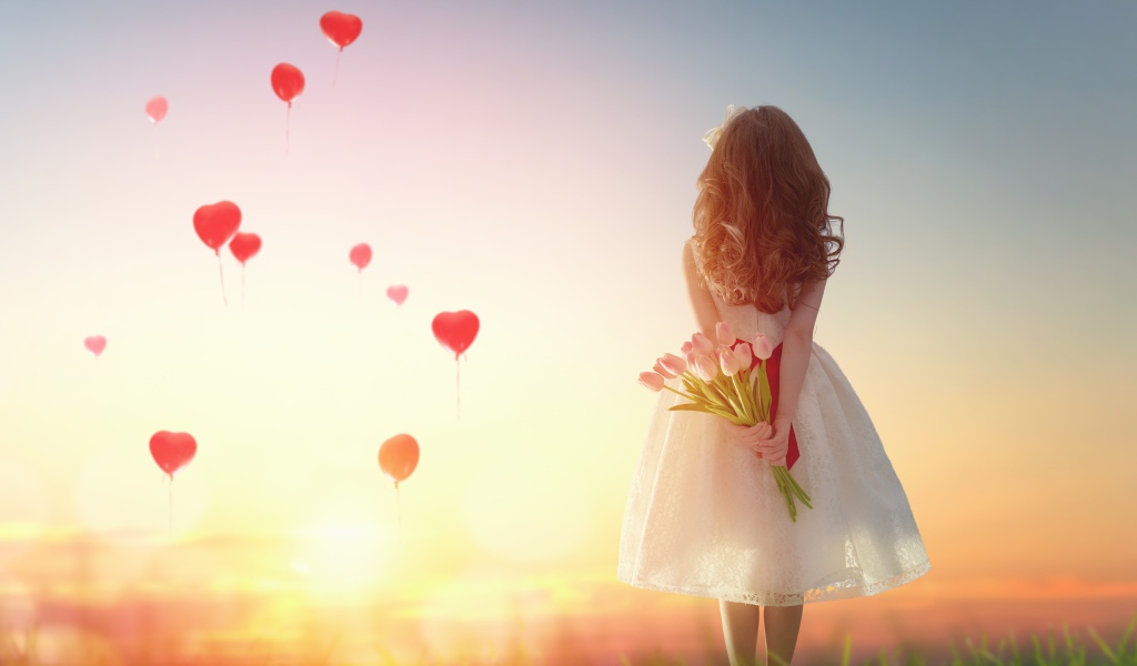 Маленькая девочка с букетом тюльпанов на фоне неба с воздушными шарами