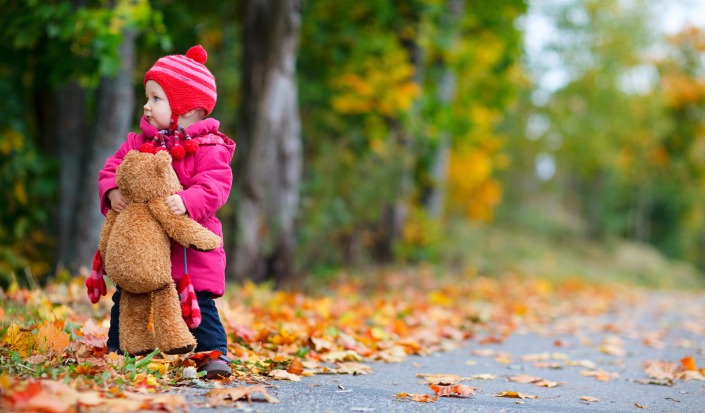 Маленькая девочка с медвежонком на дороге осенью 