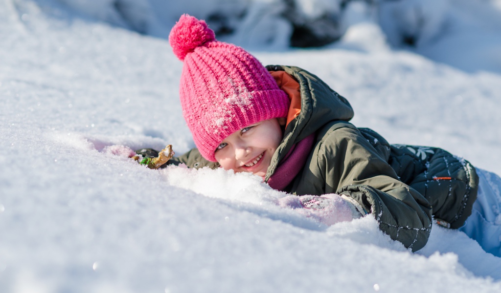 Маленькая улыбающаяся девочка лежит на снегу