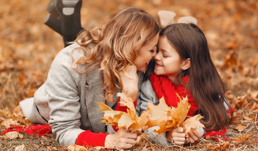 Мама с дочкой лежат на листве осенью 