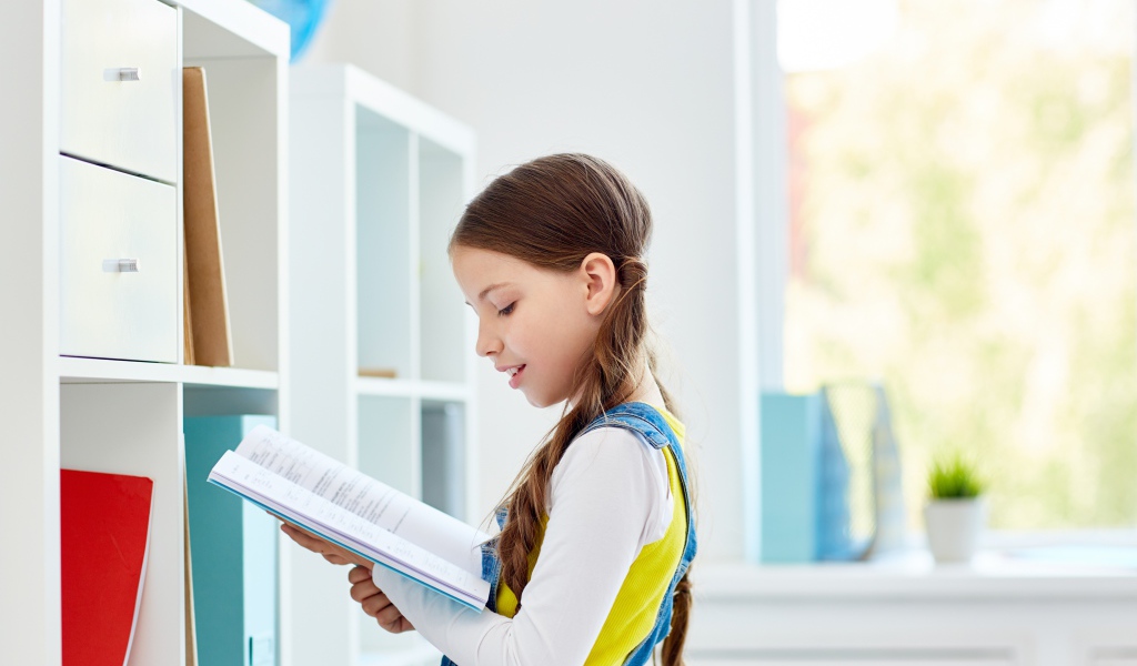 Умная девочка школьница с книгой в библиотеке 