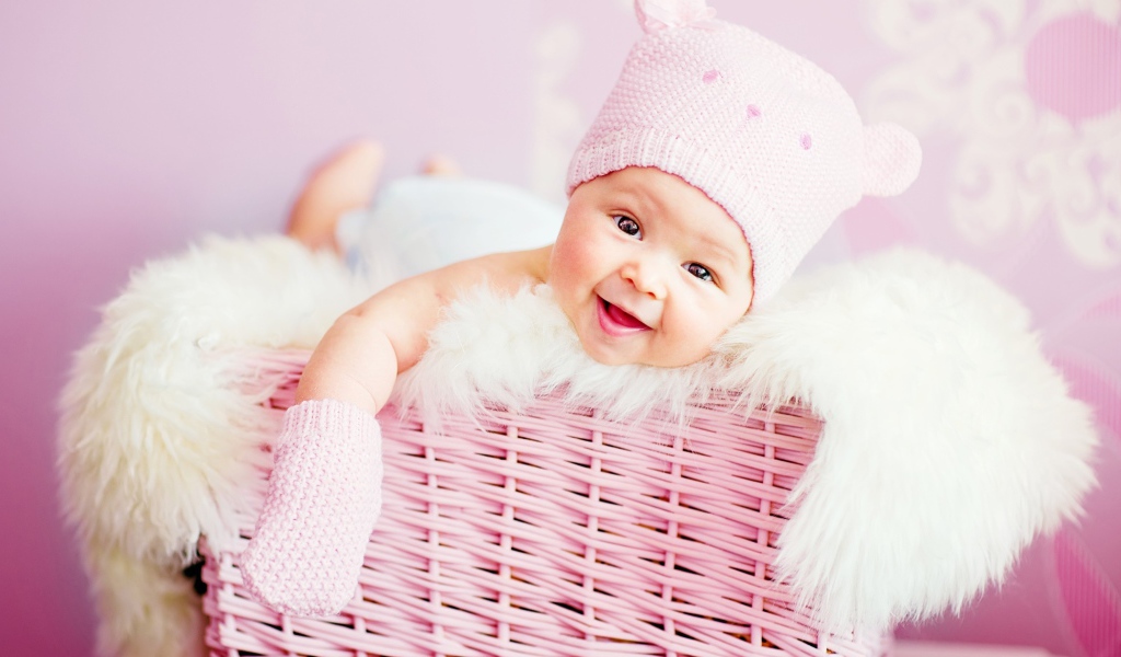 Улыбающийся грудной ребенок в шапке в розовой корзине 