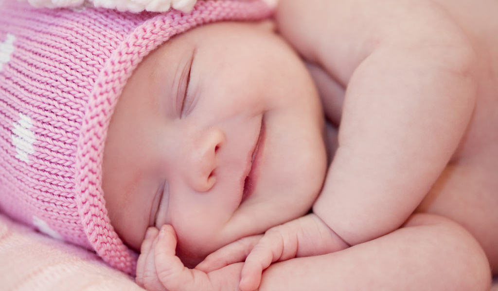 Улыбающийся грудной ребенок в розовой вязаной шапке 