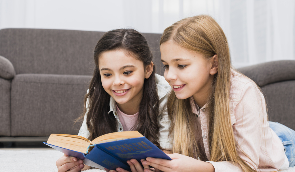 Две маленькие девочки читают книгу на полу