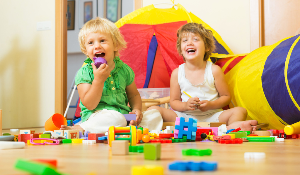 Два улыбающихся ребенка играют с конструктором 