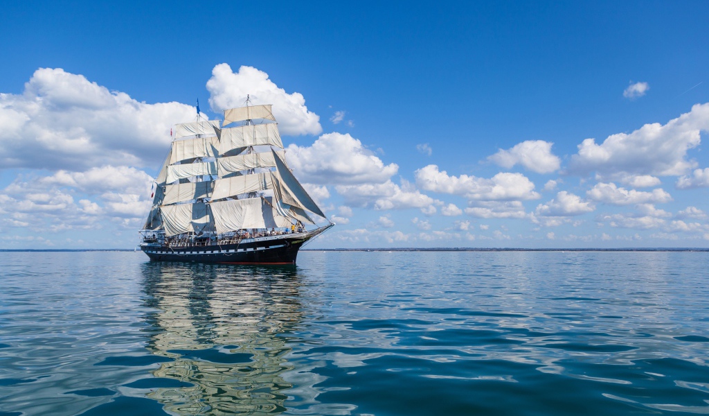 Большой корабль с белыми парусами в море под голубым небом