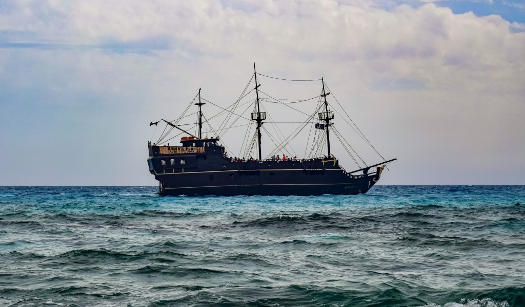 Большой черный пиратский корабль с опущенными парусами в море 