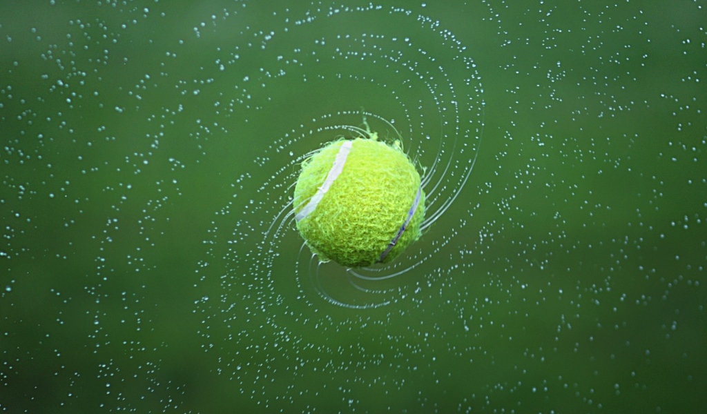 Теннисный мяч в брызгах воды на зеленом фоне