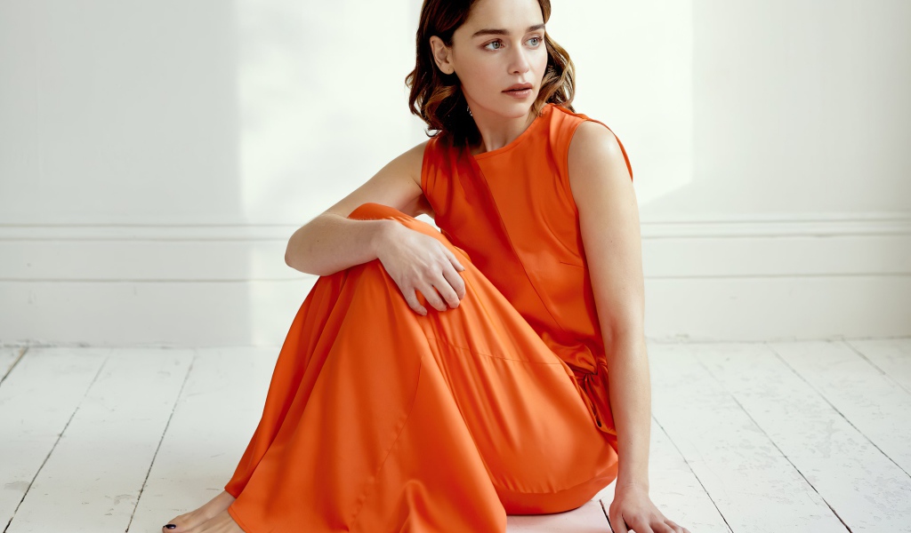 Актриса Эмилия Кларк  в оранжевом платье сидит на полу