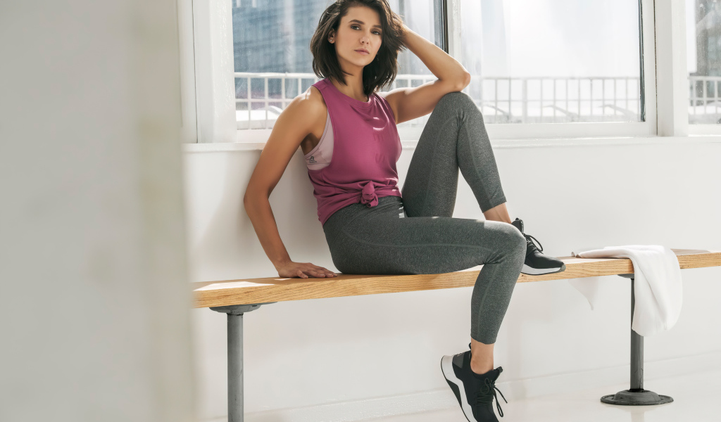 Актриса Нина Добрев сидит на лавке в спортивном костюме