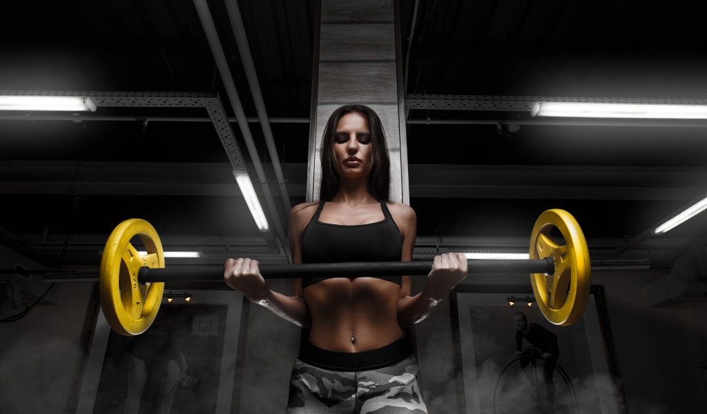 Спортивная стройная девушка поднимает штангу