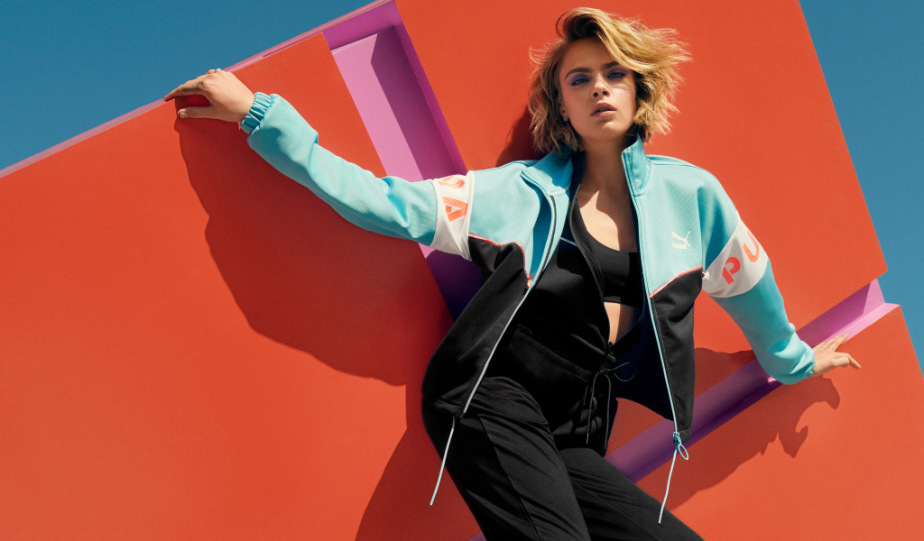 Красивая актриса Кара Делевинь в спортивном костюме у стены 