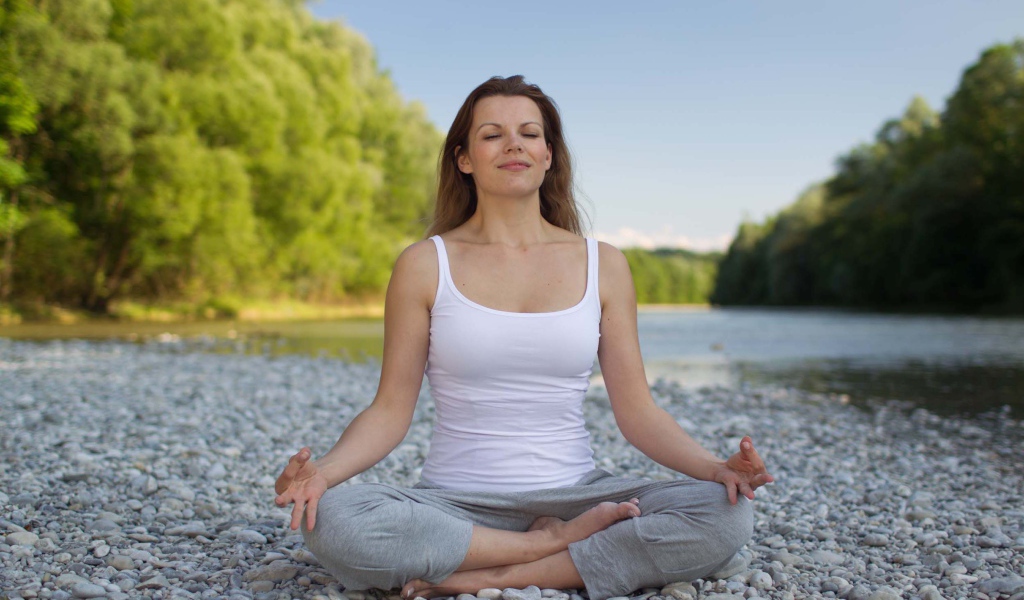 Девушка в позе лотоса медитирует у реки 