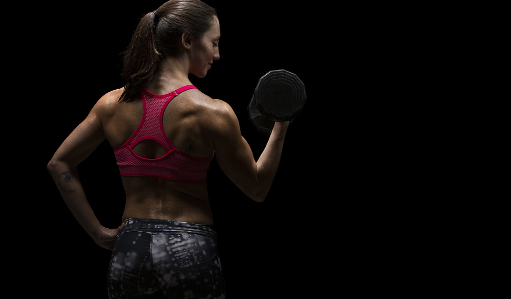 Девушка качает руки гантелей на черном фоне 