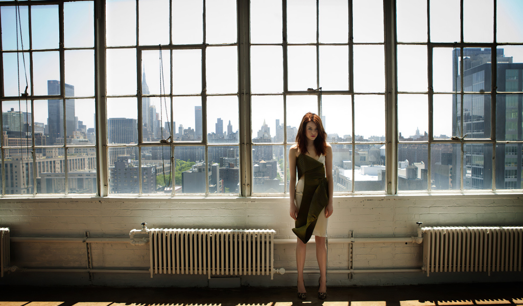 Популярная актриса Эмма Стоун стоит у большого окна