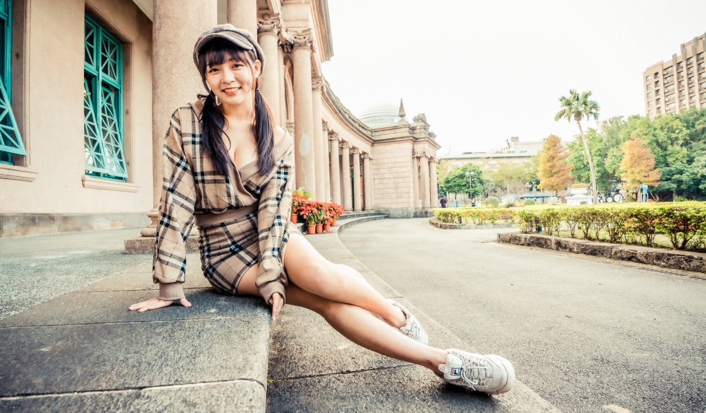 Улыбающаяся азиатка в кепке сидит на ступеньках 