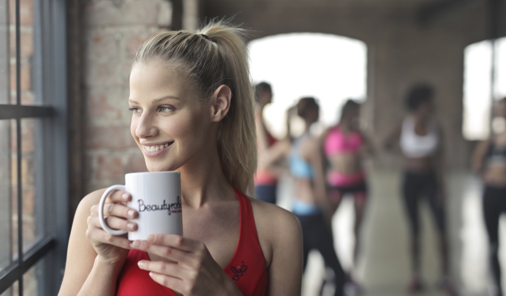 Улыбающаяся спортивная девушка с чашкой кофе у окна