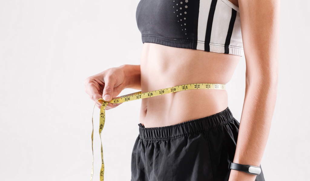 Спортивная девушка меряет талию сантиметром 