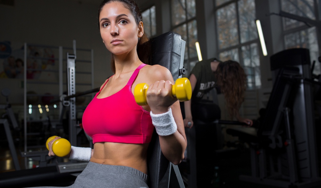 Спортивная девушка качает руки желтыми гантелями в спортзале