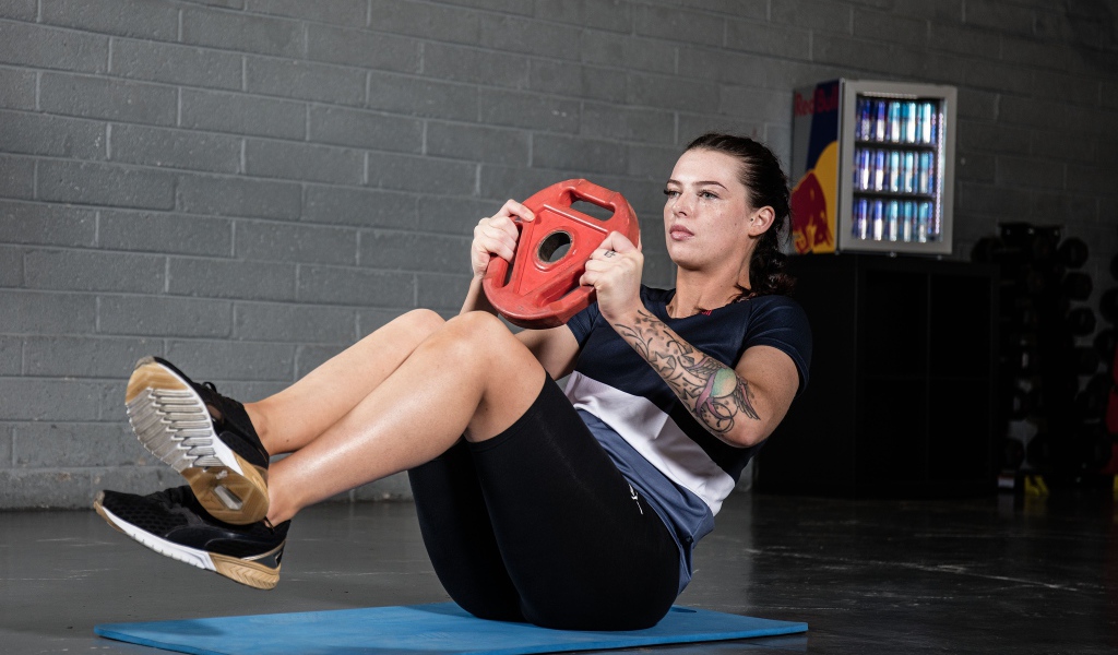 Сильная девушка с татуировками на руке качает пресс 