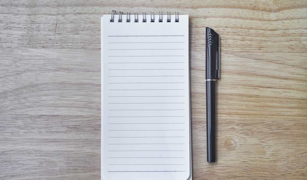 Авторучка и блокнот лежат на деревянном столе