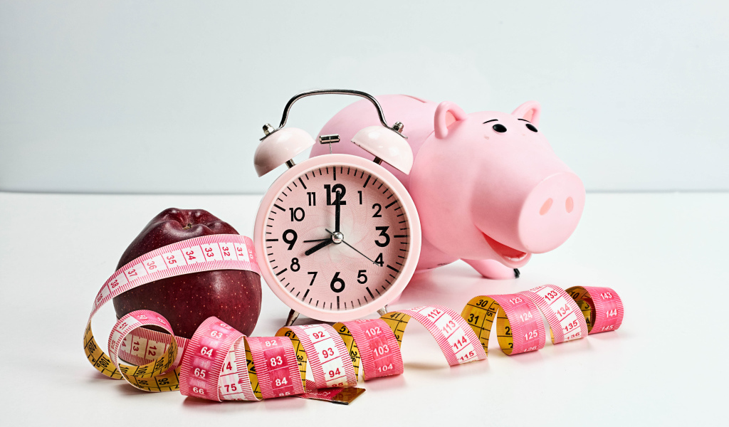 Будильник, свинья копилка, яблоко и сантиметр на белом фоне